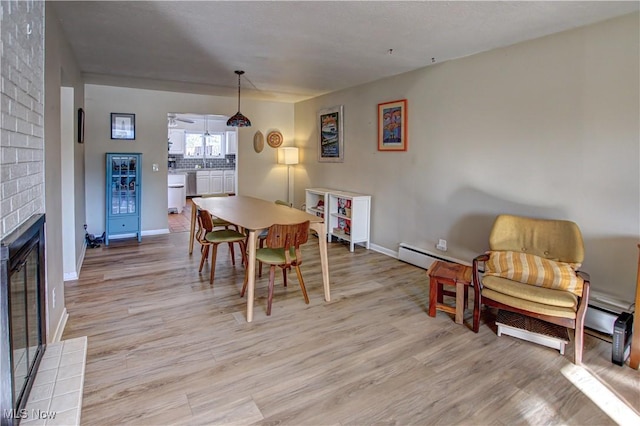 dining area featuring light wood-style floors, a fireplace, baseboards, and a baseboard heating unit