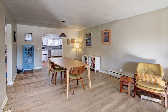 dining room with light wood-style floors, baseboards, baseboard heating, and a textured ceiling