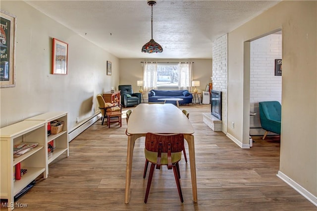 dining room featuring a baseboard radiator, a brick fireplace, a textured ceiling, and wood finished floors