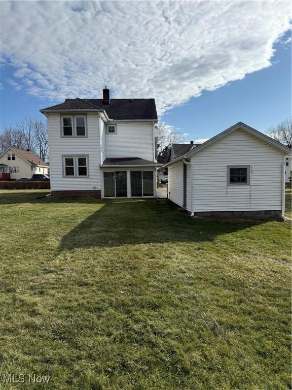 rear view of property featuring a sunroom, a chimney, and a yard