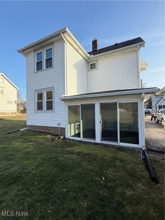 back of house with a lawn, a chimney, and a sunroom