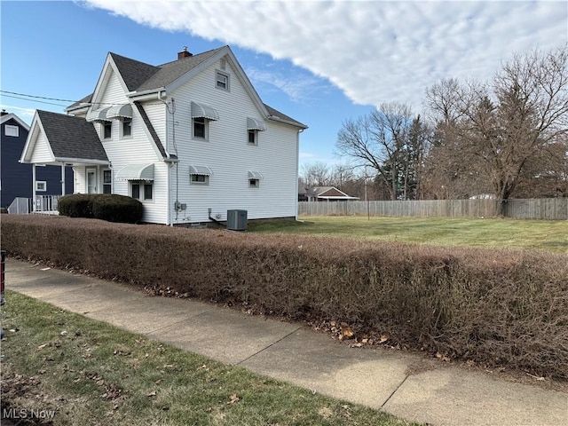 view of side of home with a lawn, a chimney, roof with shingles, fence, and central air condition unit