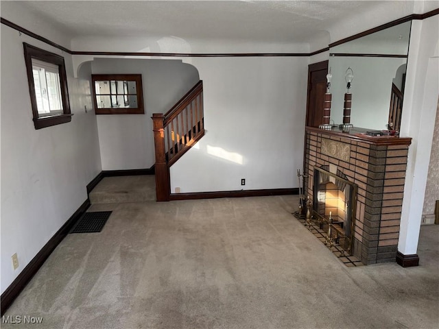 unfurnished living room with a brick fireplace, carpet, stairway, and baseboards