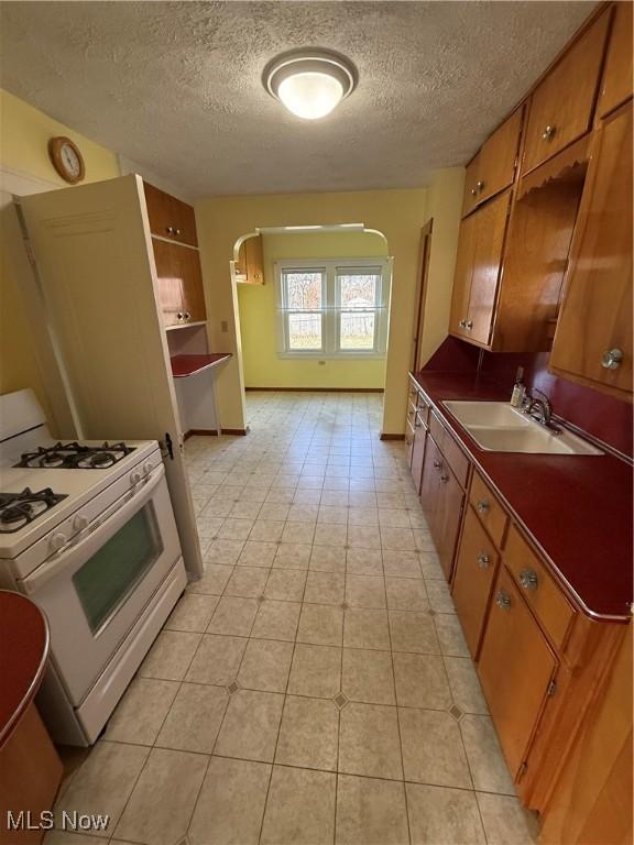 kitchen featuring dark countertops, brown cabinets, a textured ceiling, white gas stove, and a sink