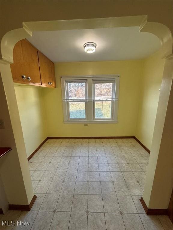 interior space with arched walkways, light tile patterned flooring, and baseboards