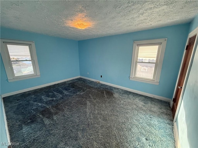 unfurnished room featuring a textured ceiling, dark carpet, and baseboards