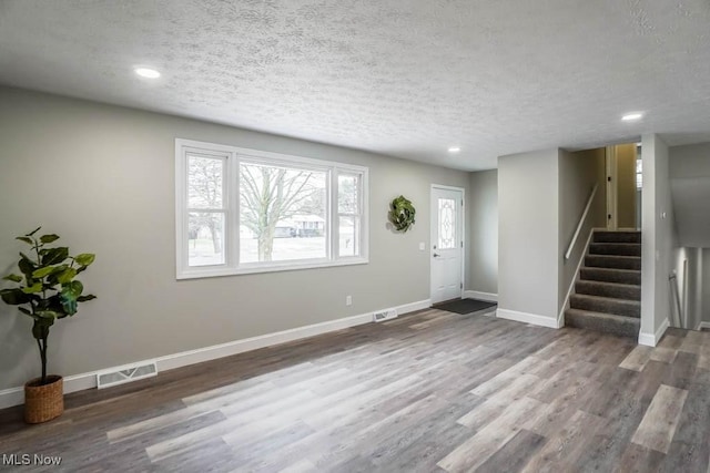 entrance foyer with a textured ceiling, wood finished floors, visible vents, baseboards, and stairway