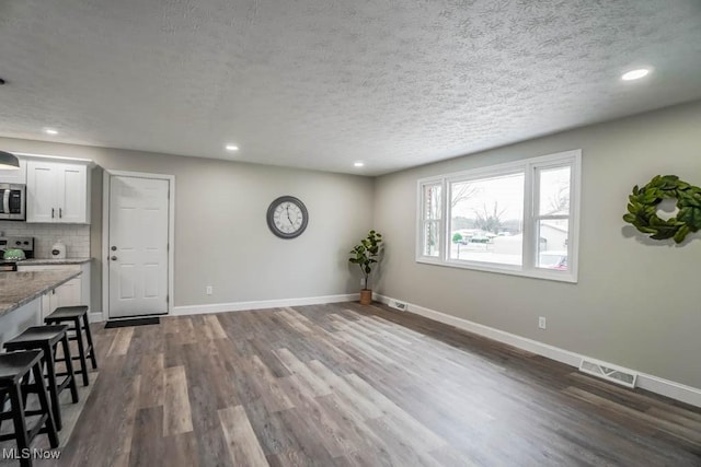 interior space featuring visible vents, baseboards, dark wood-style flooring, a textured ceiling, and recessed lighting