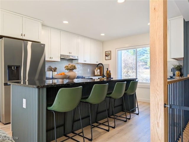 kitchen featuring light wood-type flooring, a kitchen bar, white cabinetry, stainless steel fridge, and decorative backsplash