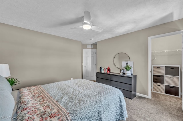 bedroom with baseboards, visible vents, a walk in closet, a textured ceiling, and carpet floors