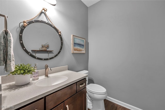 half bath with toilet, wood finished floors, vanity, and baseboards