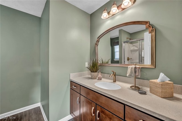 full bathroom featuring wood finished floors, a shower stall, vanity, and baseboards