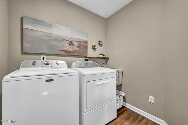 clothes washing area featuring laundry area, baseboards, washing machine and clothes dryer, and wood finished floors