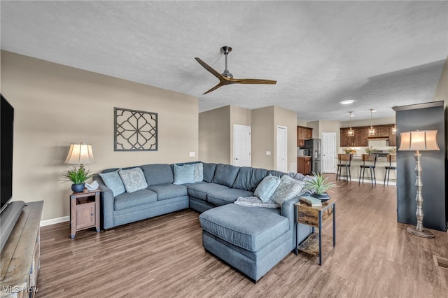 living room with ceiling fan, a textured ceiling, baseboards, and wood finished floors