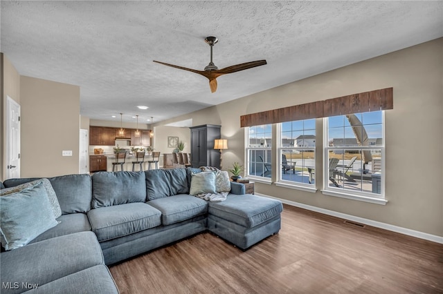 living area with a textured ceiling, wood finished floors, a ceiling fan, visible vents, and baseboards