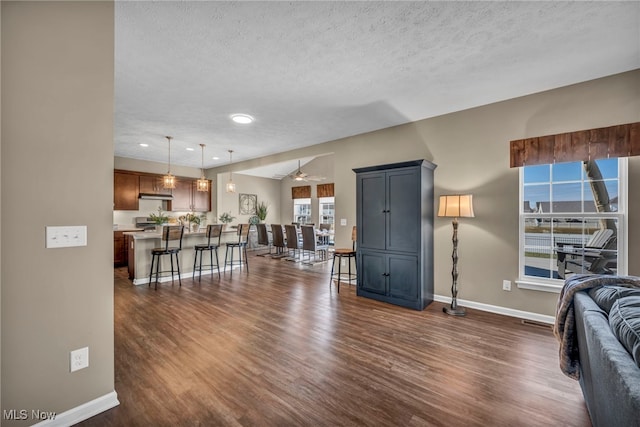 living area with a textured ceiling, ceiling fan, recessed lighting, dark wood-type flooring, and baseboards