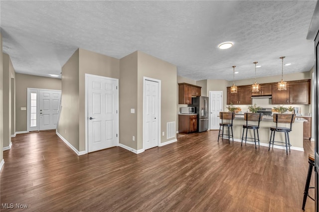 kitchen with under cabinet range hood, stainless steel appliances, visible vents, a kitchen breakfast bar, and dark wood-style floors