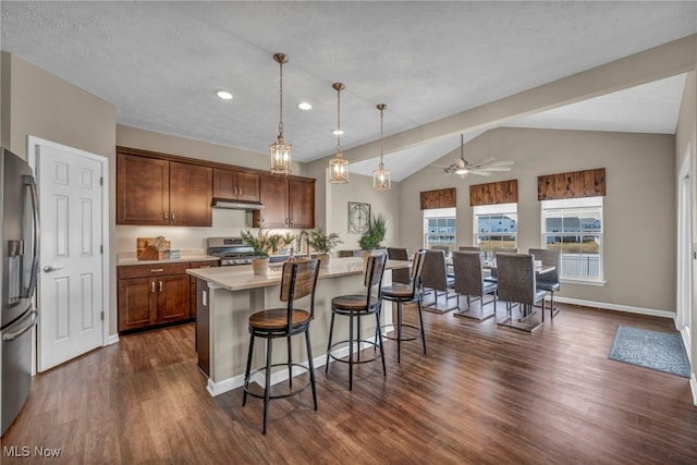 kitchen featuring dark wood finished floors, a breakfast bar area, appliances with stainless steel finishes, vaulted ceiling, and light countertops