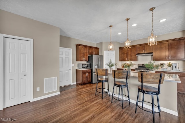 kitchen featuring dark wood finished floors, a breakfast bar area, visible vents, appliances with stainless steel finishes, and under cabinet range hood