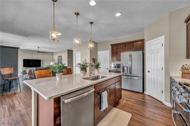 kitchen with dark wood-style floors, stainless steel appliances, a sink, and a kitchen island with sink