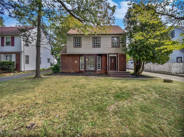 colonial house featuring brick siding, a front lawn, and fence