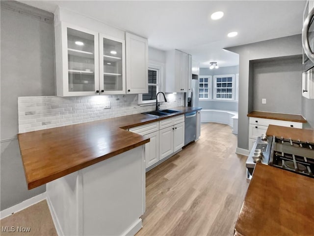 kitchen with stainless steel appliances, wooden counters, glass insert cabinets, white cabinetry, and a sink