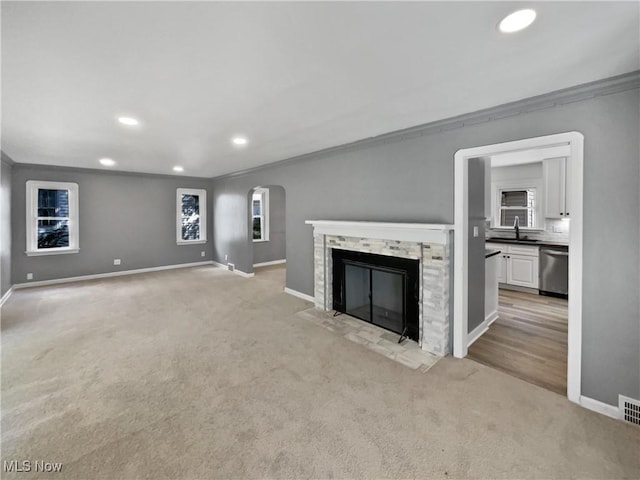 unfurnished living room with arched walkways, a stone fireplace, a sink, and light colored carpet