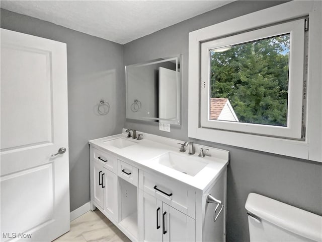 bathroom with toilet, double vanity, baseboards, and a sink