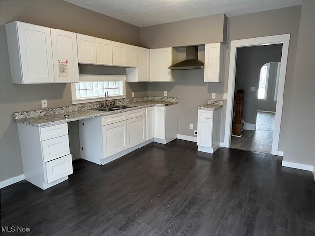 kitchen with arched walkways, dark wood finished floors, white cabinetry, a sink, and wall chimney exhaust hood