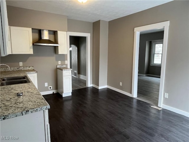 kitchen with arched walkways, a sink, white cabinets, wall chimney exhaust hood, and dark wood finished floors