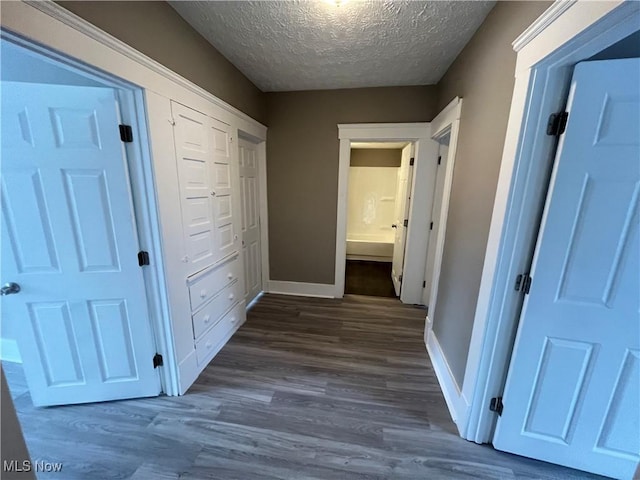 hall with dark wood-style floors, a textured ceiling, and baseboards