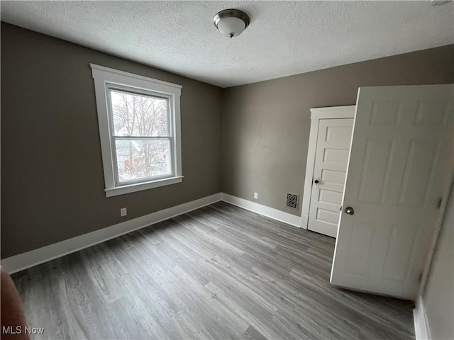 spare room with visible vents, a textured ceiling, baseboards, and wood finished floors