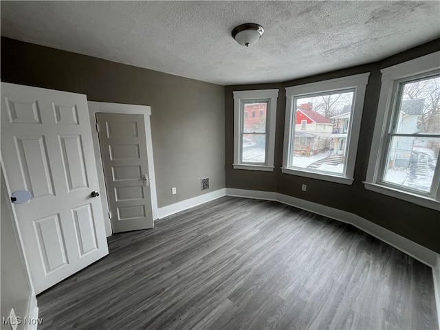 spare room with visible vents, a textured ceiling, baseboards, and dark wood-type flooring