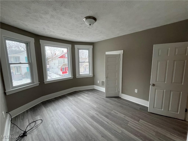 empty room with dark wood-style flooring, visible vents, a textured ceiling, and baseboards