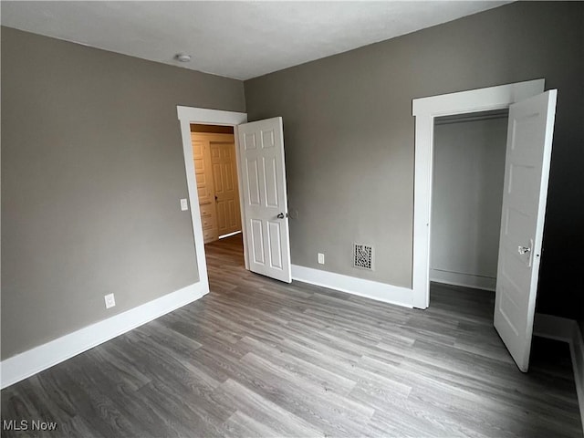 unfurnished bedroom with a closet, wood finished floors, visible vents, and baseboards