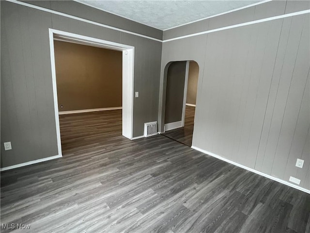 unfurnished room featuring arched walkways, wood finished floors, visible vents, and baseboards