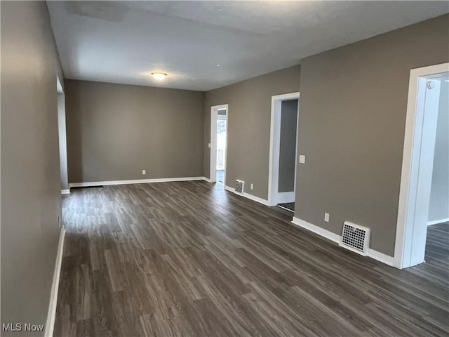 unfurnished room featuring dark wood-style floors, visible vents, and baseboards