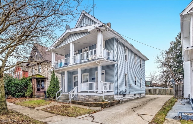 view of front of house featuring a porch, a chimney, fence, and a balcony