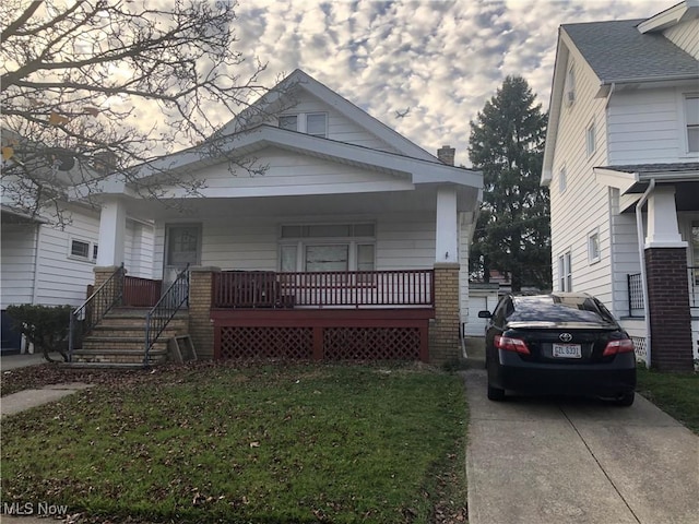 view of front facade with driveway, a chimney, covered porch, a front yard, and brick siding