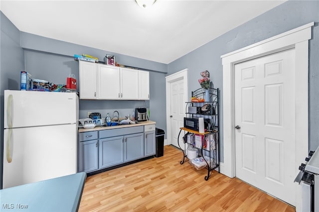 kitchen with white cabinets, freestanding refrigerator, light countertops, light wood-style floors, and a sink