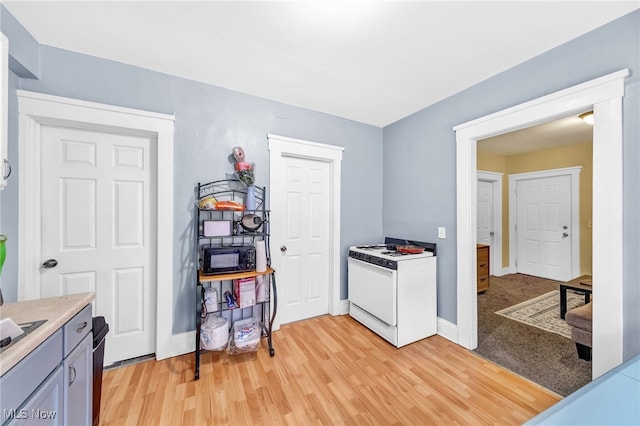 kitchen with light countertops, black microwave, light wood-type flooring, white range with gas stovetop, and baseboards