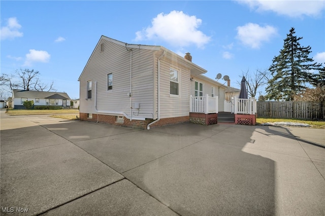 view of side of home featuring a deck, a patio, a chimney, and fence