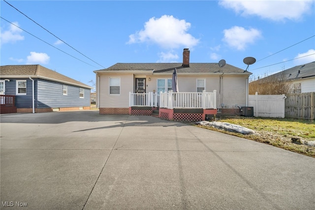 ranch-style home featuring a chimney, concrete driveway, fence, a deck, and cooling unit