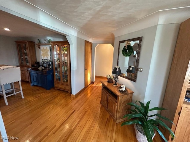 hall with arched walkways, baseboards, and light wood finished floors