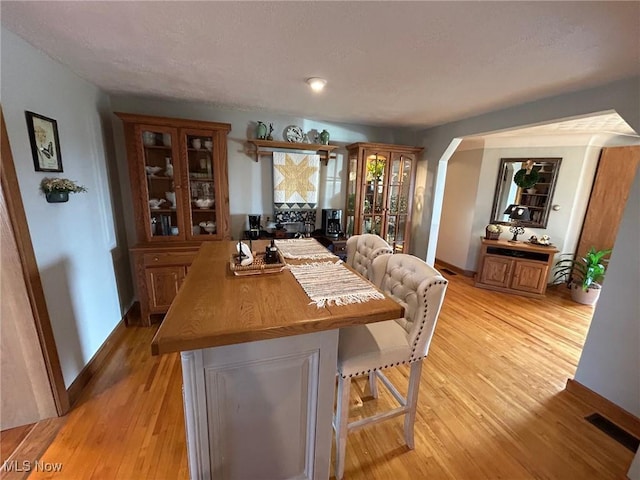 dining area with light wood-style flooring, visible vents, arched walkways, and baseboards