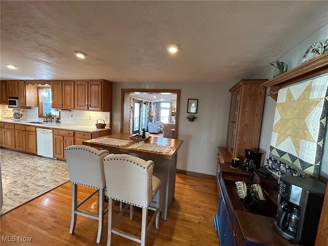 kitchen featuring white dishwasher, a sink, light wood-style floors, brown cabinetry, and stainless steel microwave