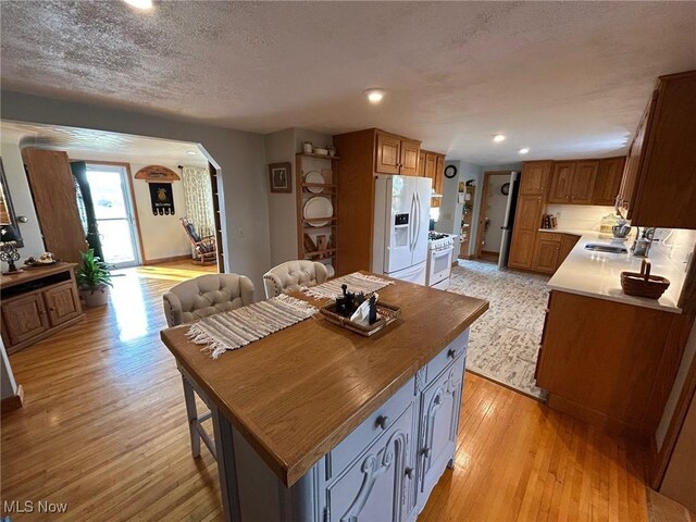 kitchen with arched walkways, a textured ceiling, light wood-style flooring, white appliances, and a sink