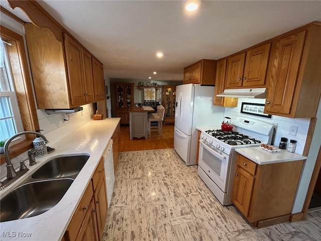 kitchen with white appliances, under cabinet range hood, brown cabinets, and a sink