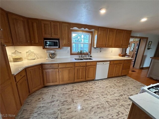 kitchen featuring brown cabinetry, dishwasher, stainless steel microwave, light countertops, and a sink