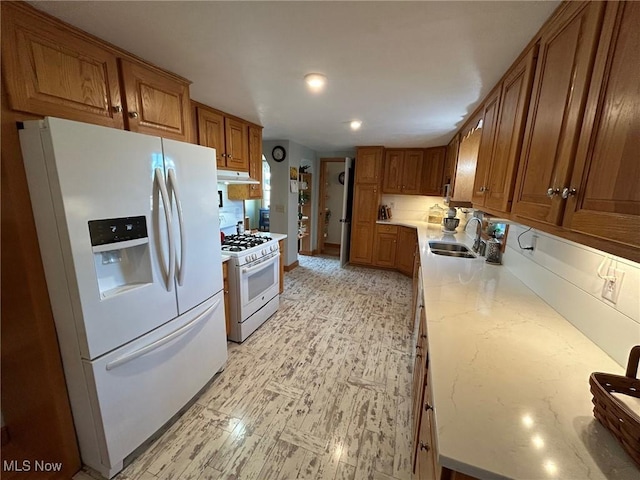 kitchen featuring brown cabinetry, white appliances, a sink, and under cabinet range hood